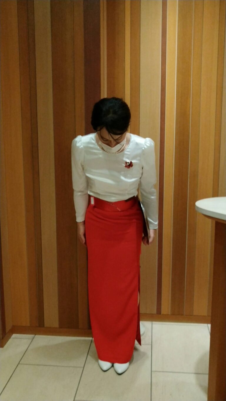 白いブラウスと赤いロングスカートでお辞儀をするバンケットコンパニオン女装